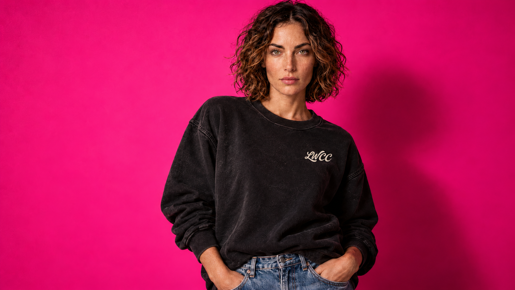 Front view of our campaign model wearing the washed charcoal sweatshirt with the cream LWCC chest logo against electric pink