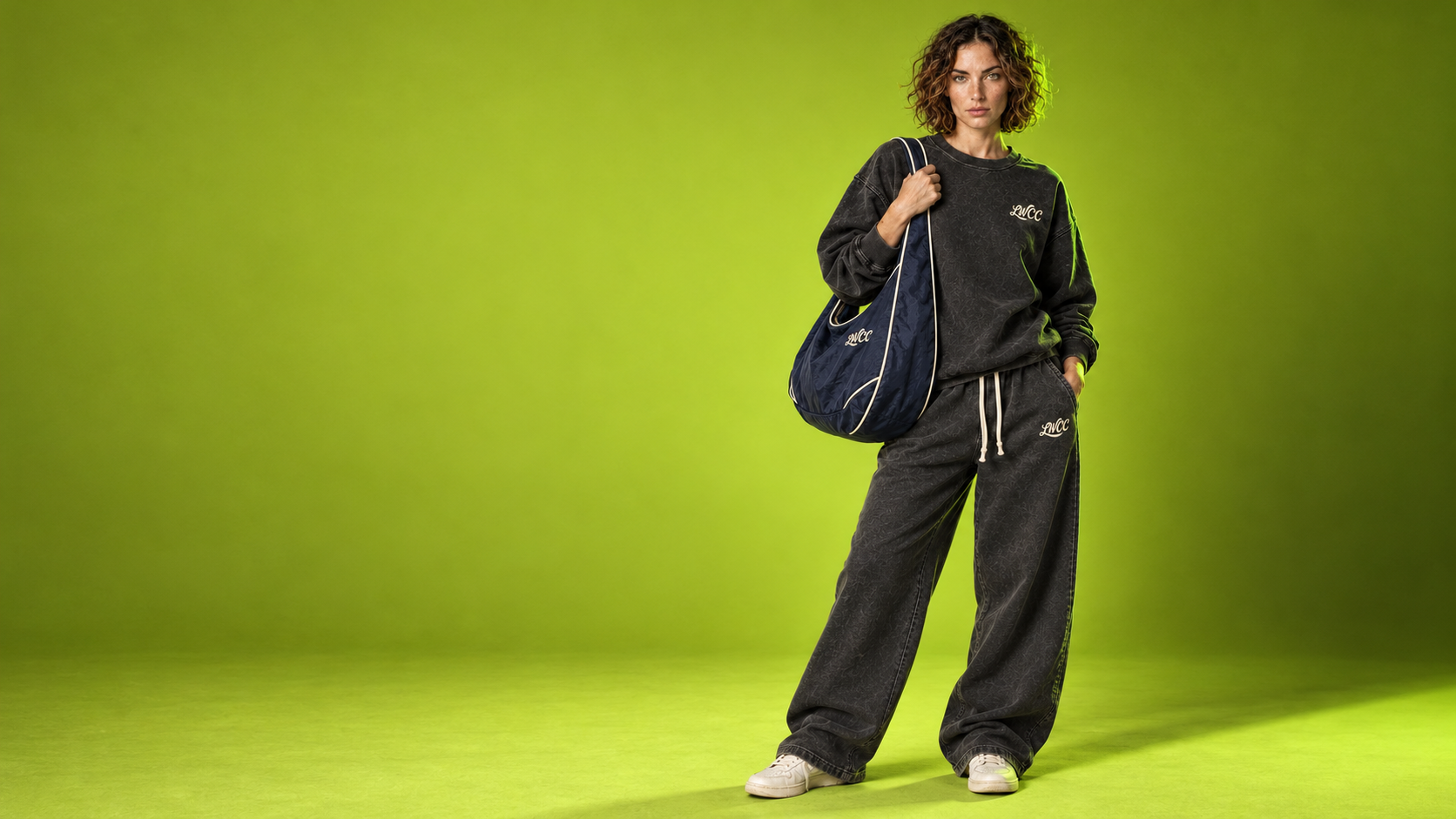 Lost Wight model wearing charcoal baggy sweats and carrying the navy Seafront shoulder bag against neon green