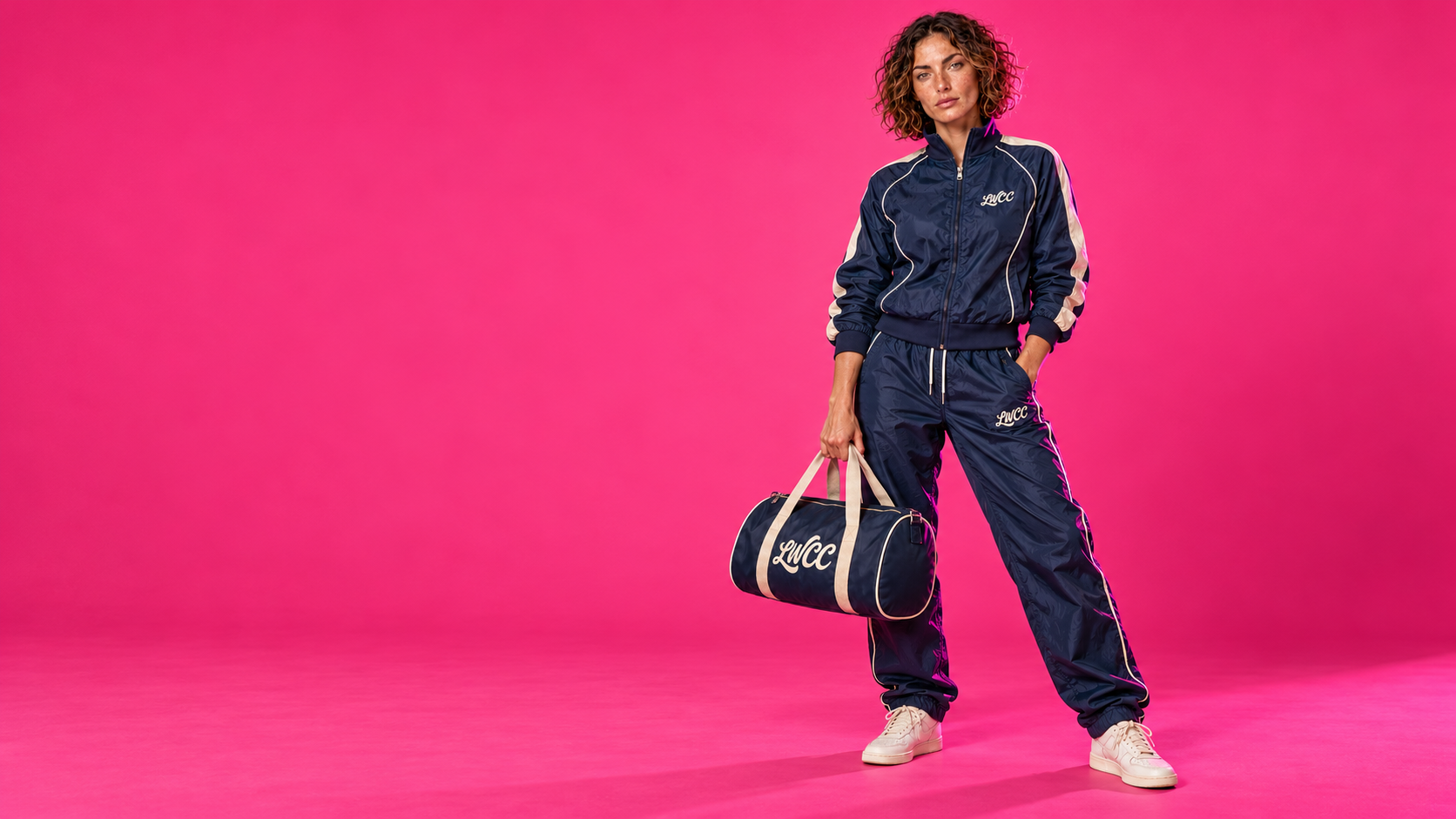 Lost Wight model wearing the navy Court Piping shell suit and carrying the cream-trimmed bowling bag against neon pink