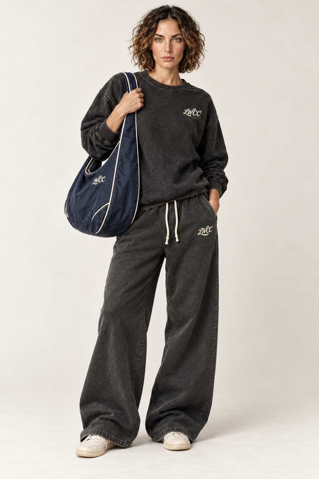 Lost Wight model in charcoal baggy straight-leg sweatpants carrying the navy Seafront bag